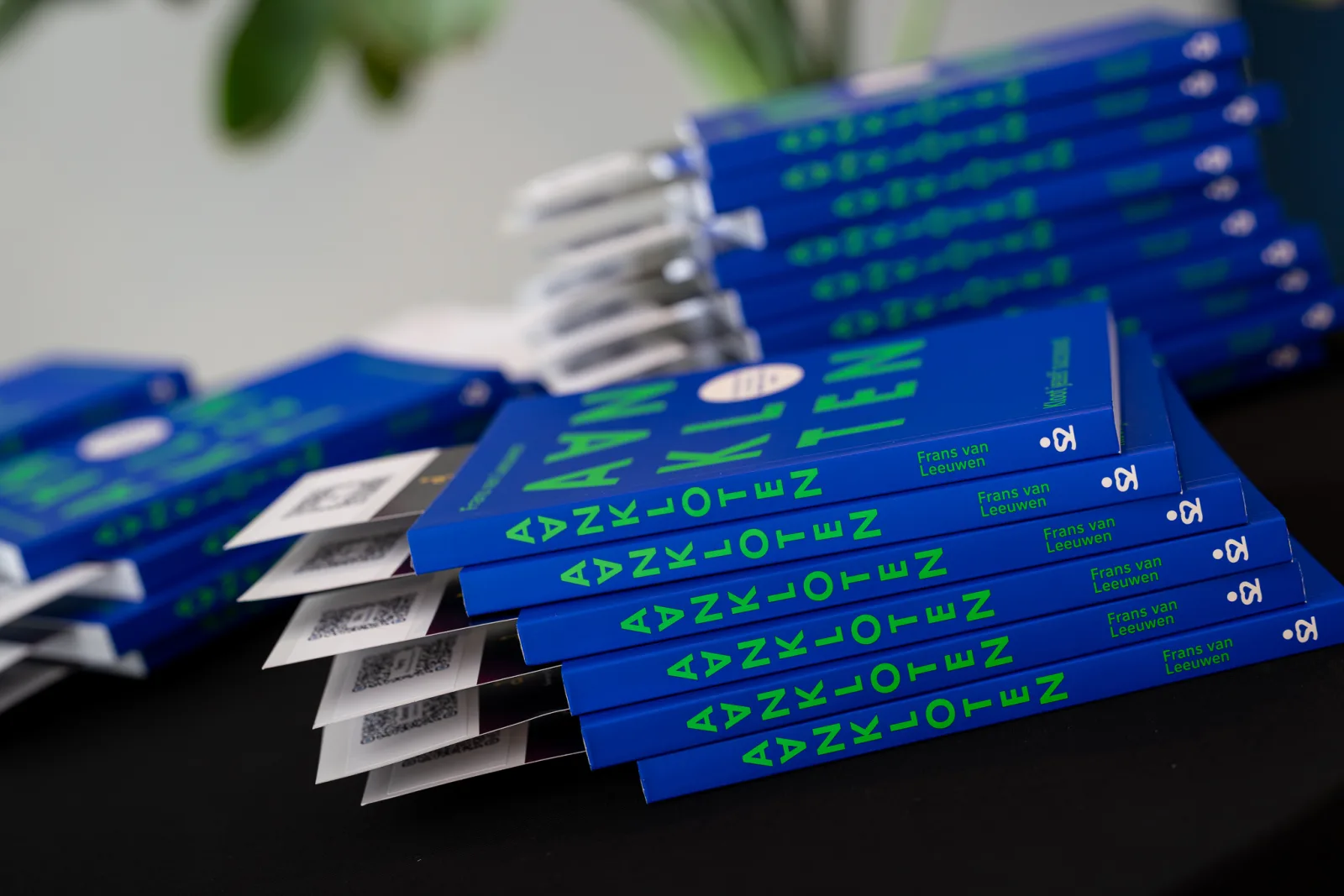 Stapel blauwe boeken 'Aankloten' van Frans van Leeuwen met LemonPress-boekenleggers en QR-codes