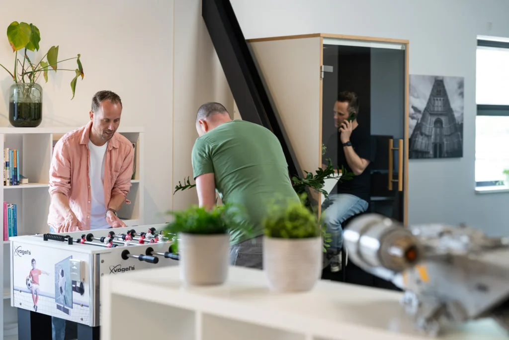 Twee collega's spelen tafelvoetbal terwijl een collega belt in de telefooncel